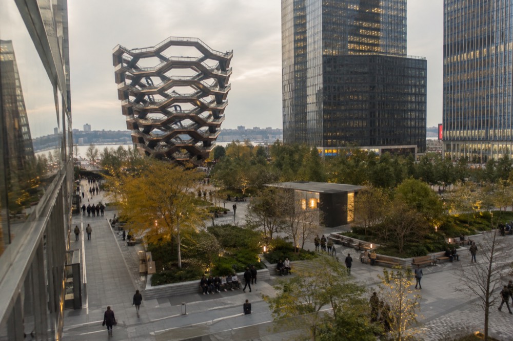 Outdoor plaza with seating and planted areas between tall office towers
