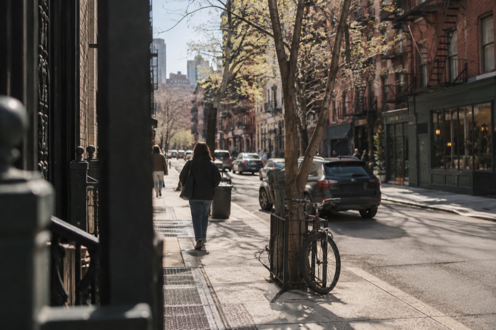 A view down a Lower East Side street with old brick tenement buildings, fire escapes and a small shop awning