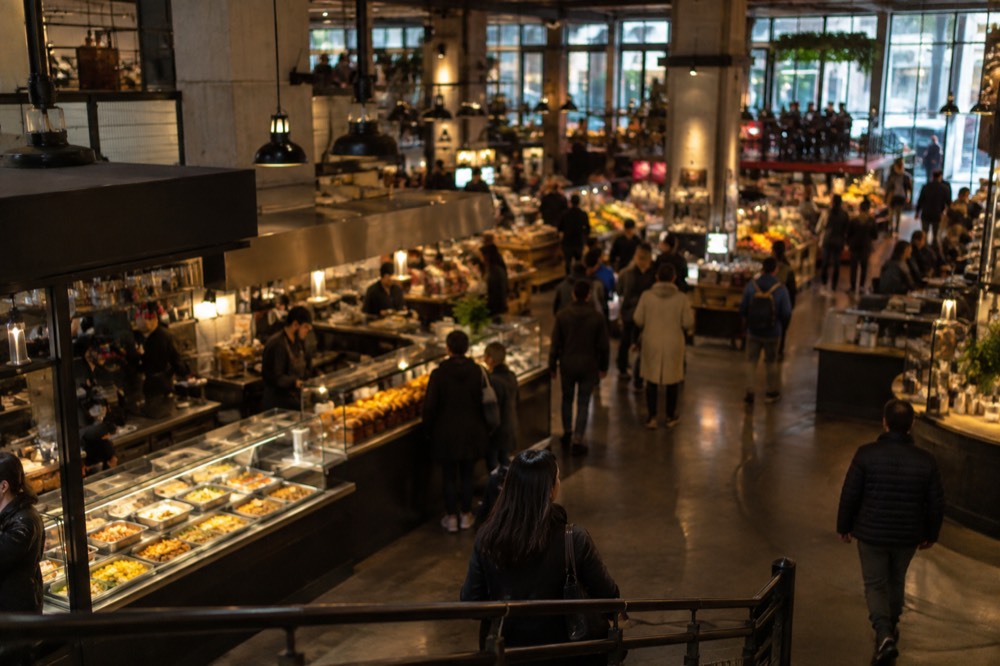 A food hall interior with vendors and counters under warm lighting and shoppers browsing