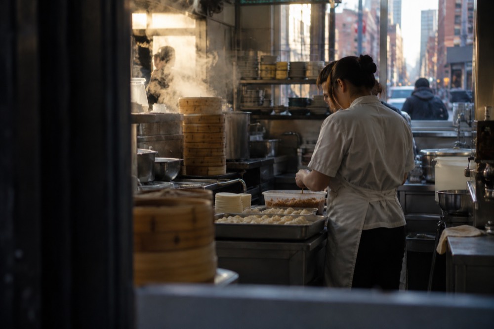 A cook working behind a counter preparing dumplings in a small busy kitchen
