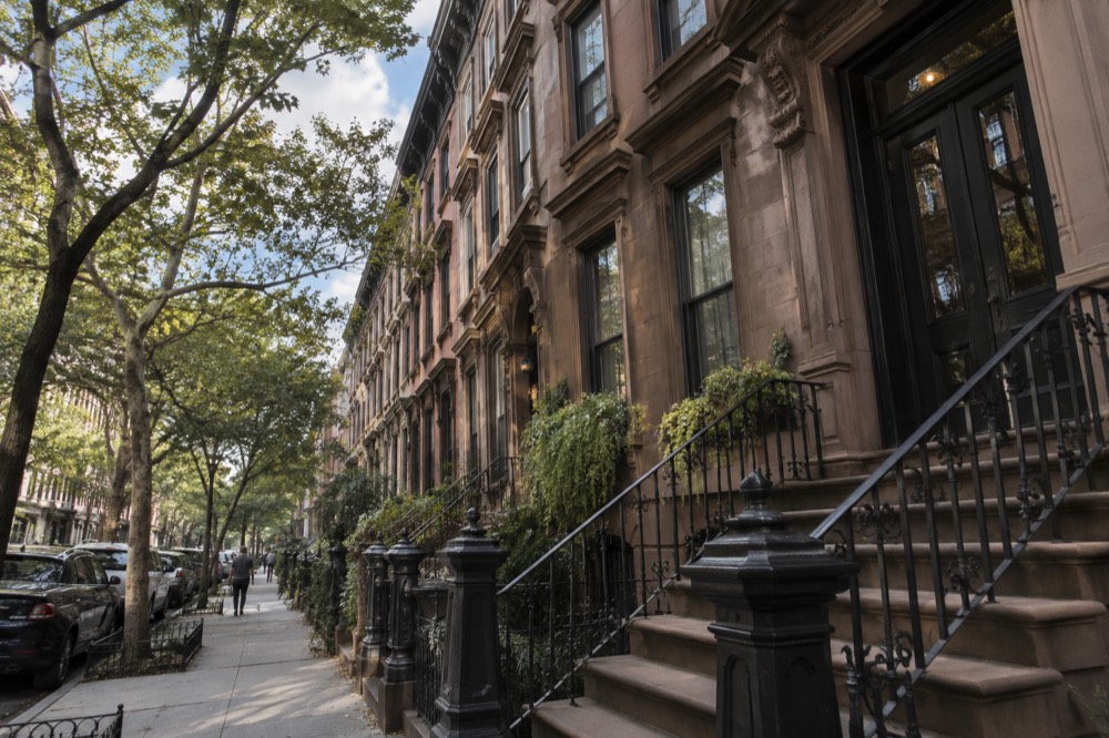 Row of brownstone townhouses with stoops on a quiet side street