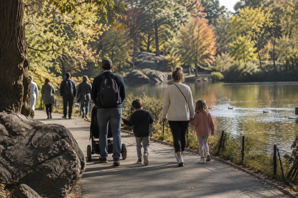 Families walking along a path near a lake in Central Park in late afternoon light