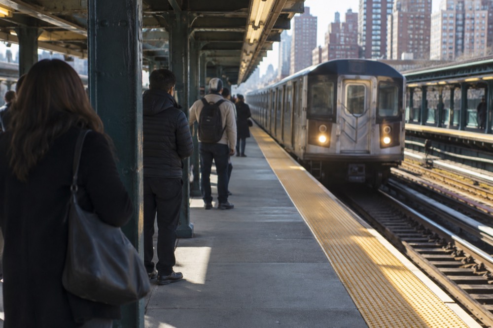 Subway platform with a train arriving and passengers waiting near a column