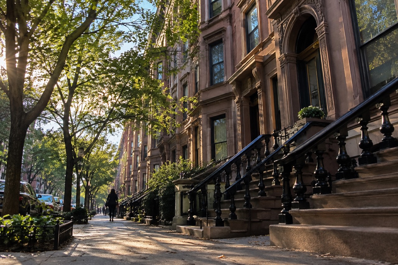 Brownstone apartment buildings lining a residential street on the Upper West Side with trees in leaf
