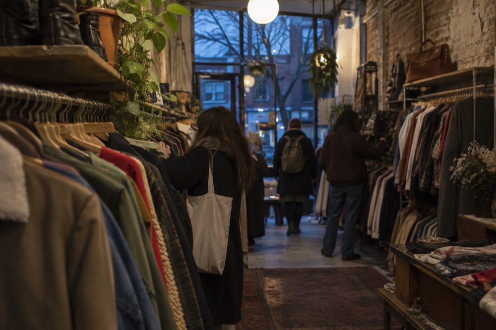 Shoppers browsing racks of secondhand clothing in a narrow vintage store