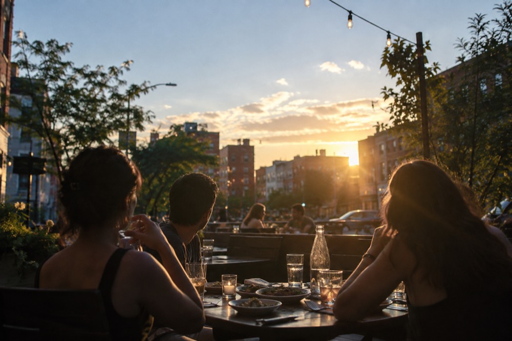 Diners at an outdoor table with small plates and drinks in the evening