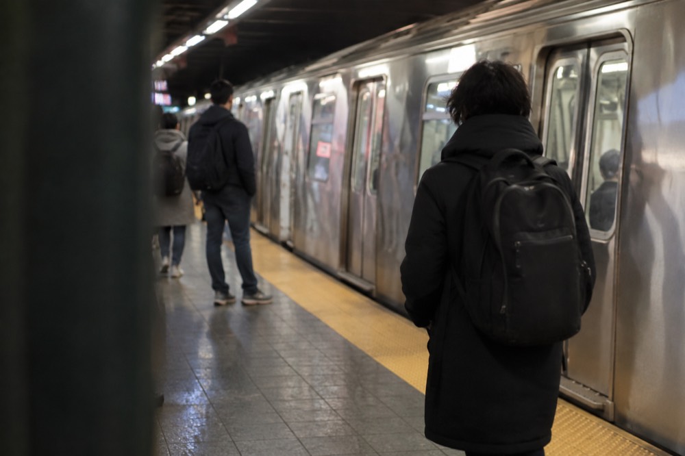 A subway platform with a waiting train and a few riders carrying backpacks