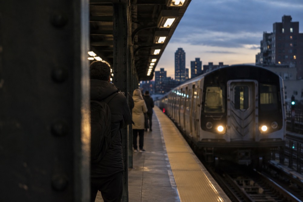 A subway platform in Brooklyn with a train pulling in during the afternoon