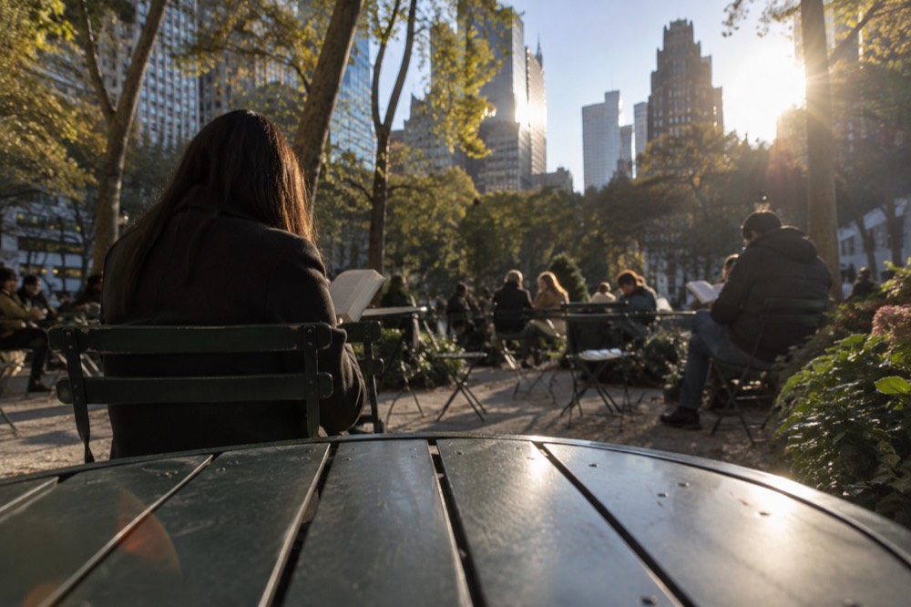 People reading at green metal tables under trees in Bryant Park
