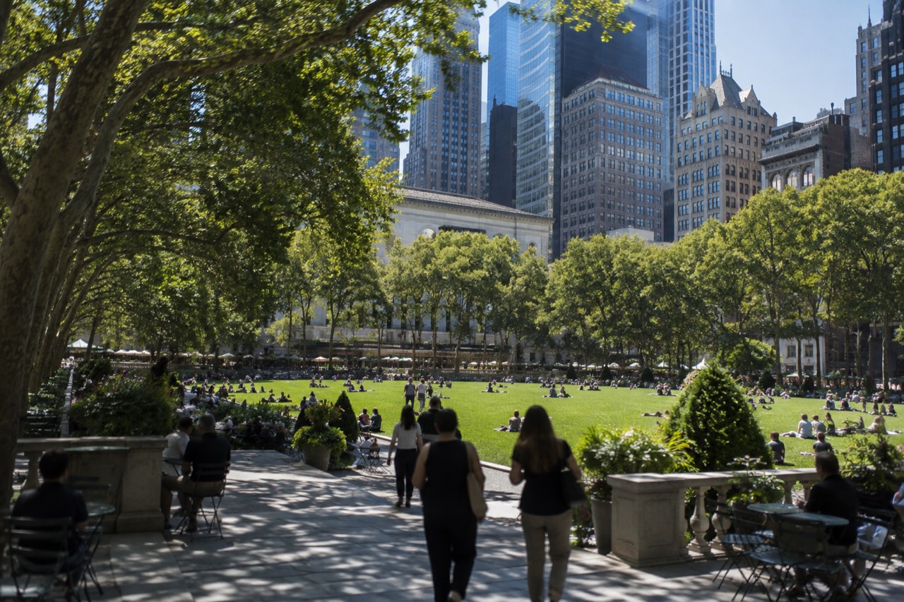 Green lawn and shade trees of Bryant Park with Midtown office towers rising behind them