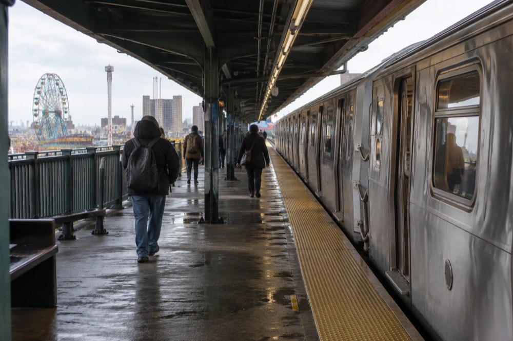 A subway platform with a train waiting under an elevated structure