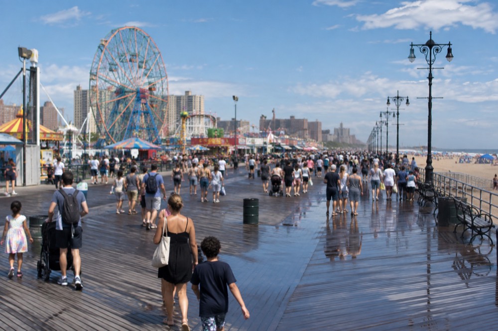 A crowded boardwalk with families and a Ferris wheel turning under a blue sky