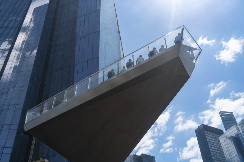 A triangular deck extending outward from a glass tower with railings and angled glass panels