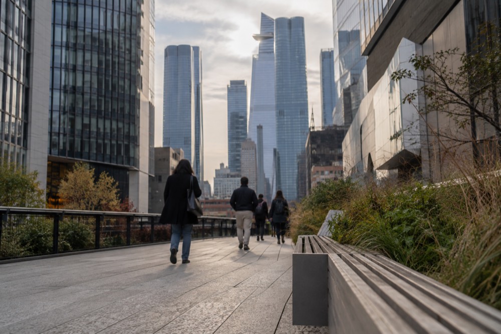An elevated park walkway passing between modern buildings toward a cluster of glass towers