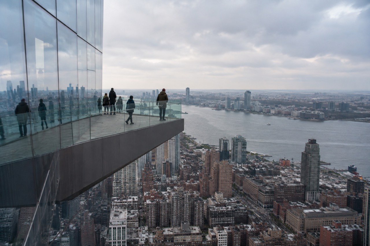 A triangular observation deck extending from a glass skyscraper above Manhattan with the Hudson River in the background