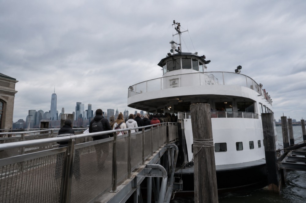 The Ellis Island ferry slip with a Statue City Cruises boat docked and passengers boarding