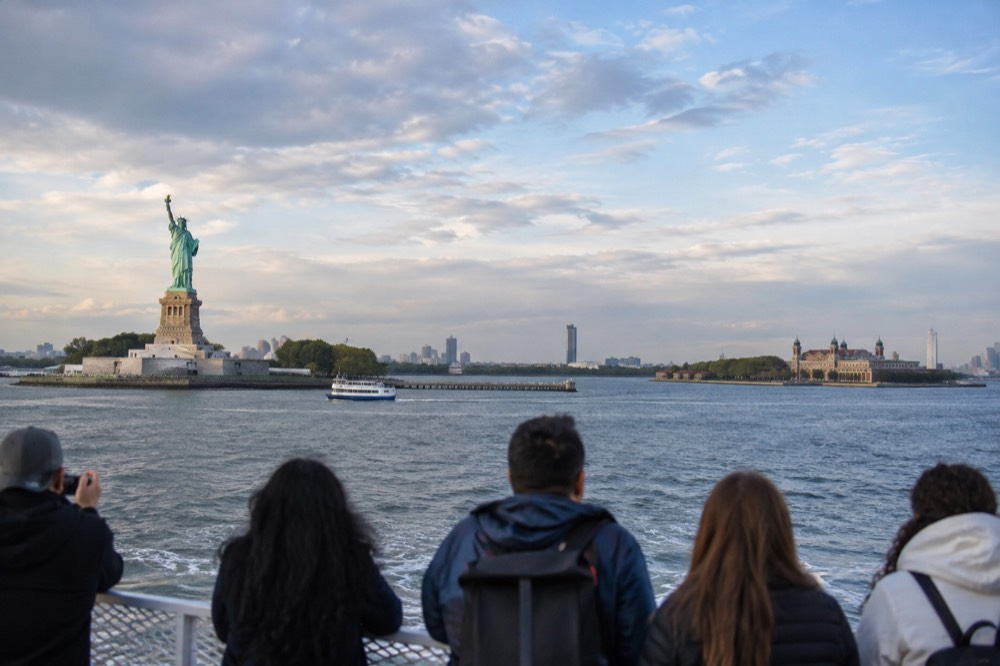 Statue of Liberty and Ellis Island seen together from a ferry deck crossing New York Harbor