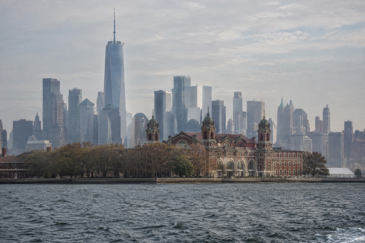 The red-brick main building of Ellis Island seen from the water, with the Manhattan skyline behind it