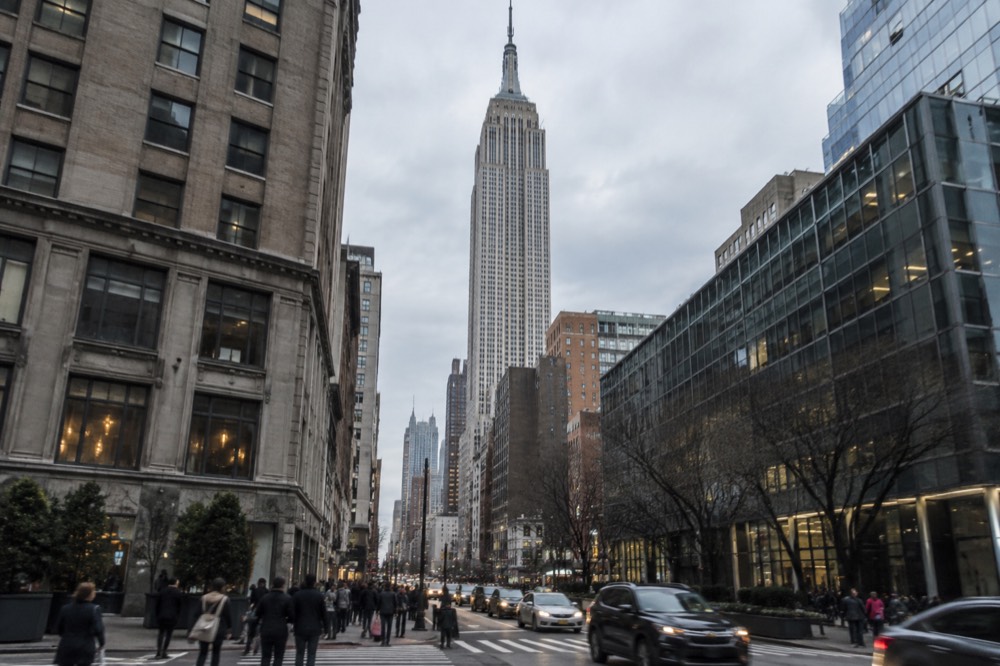 The Empire State Building tower seen from a Midtown street corner, pedestrians crossing below