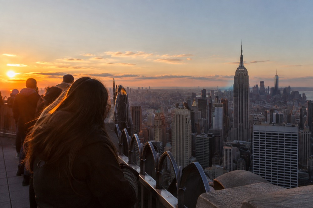 The open-air 86th floor observation deck of the Empire State Building with visitors at the rail and the Manhattan skyline beyond