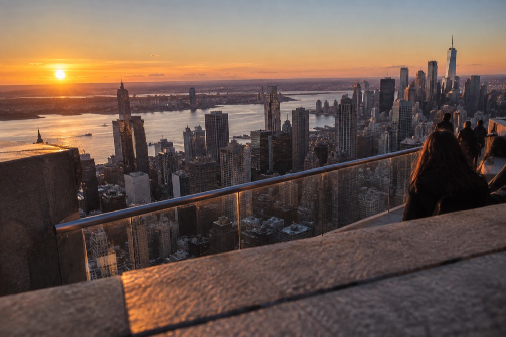 The Manhattan skyline at sunset from a high observation deck, with the Hudson River and New Jersey beyond