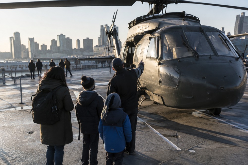 A family looking up at a helicopter on the flight deck while a guide points out its features