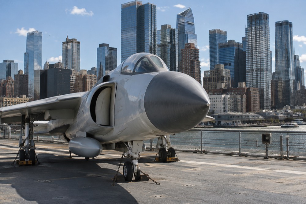 A jet aircraft on the flight deck framed against Midtown office towers across the river