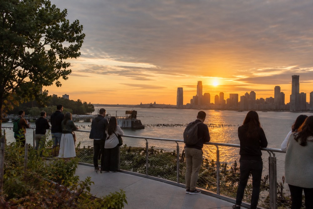 Golden sunset light over the Hudson River seen from an elevated park with visitors at the rail