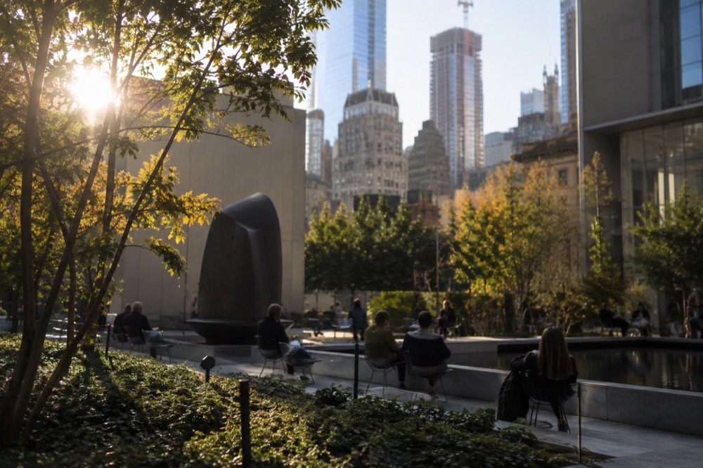 People resting on benches in an outdoor sculpture garden surrounded by tall buildings