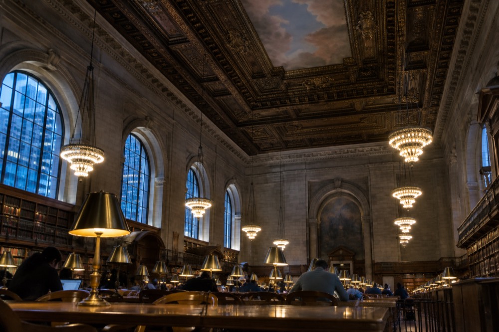 Long wooden reading tables with brass lamps under the arched ceiling and murals of the Rose Main Reading Room