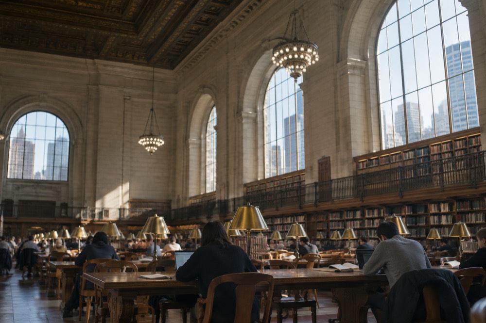 Visitors reading and working at the long tables of the main reading room under tall arched windows