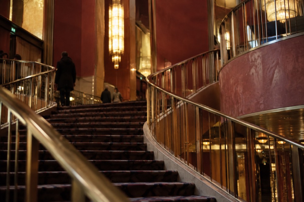 A curved staircase inside an Art Deco building with brass railings and warm lighting