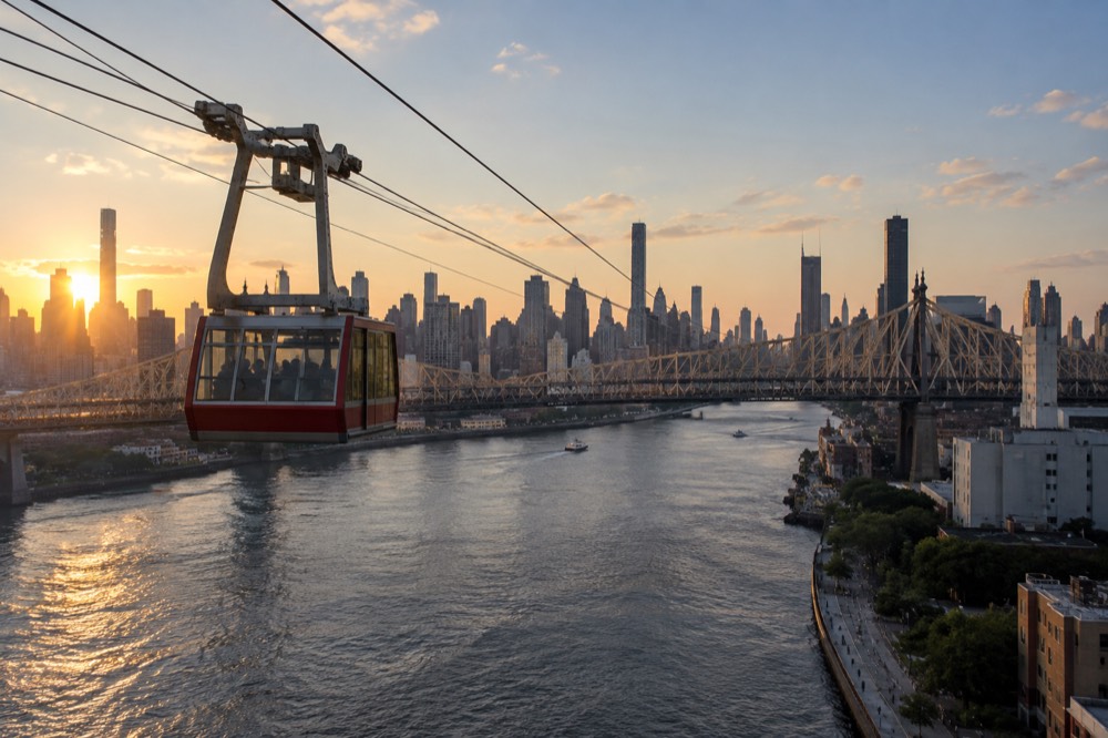 A cable tram cabin gliding over the East River toward Roosevelt Island with the Queensboro Bridge and Manhattan skyline behind it