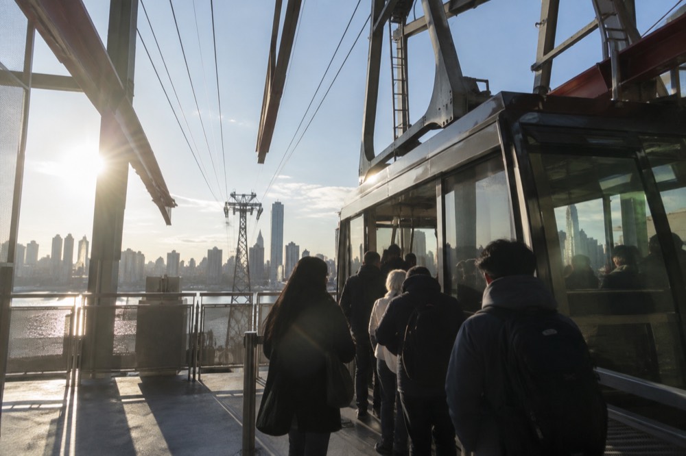 Passengers boarding a glass-walled tram cabin at the Second Avenue station on a clear morning