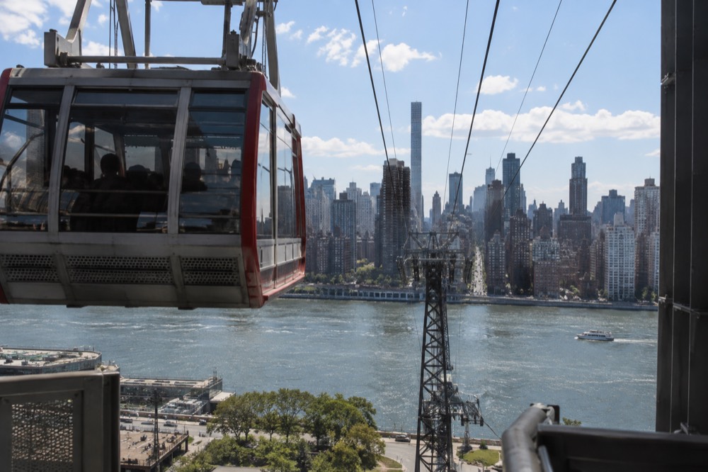 A tram cabin seen from the Roosevelt Island station platform with the Manhattan skyline across the river