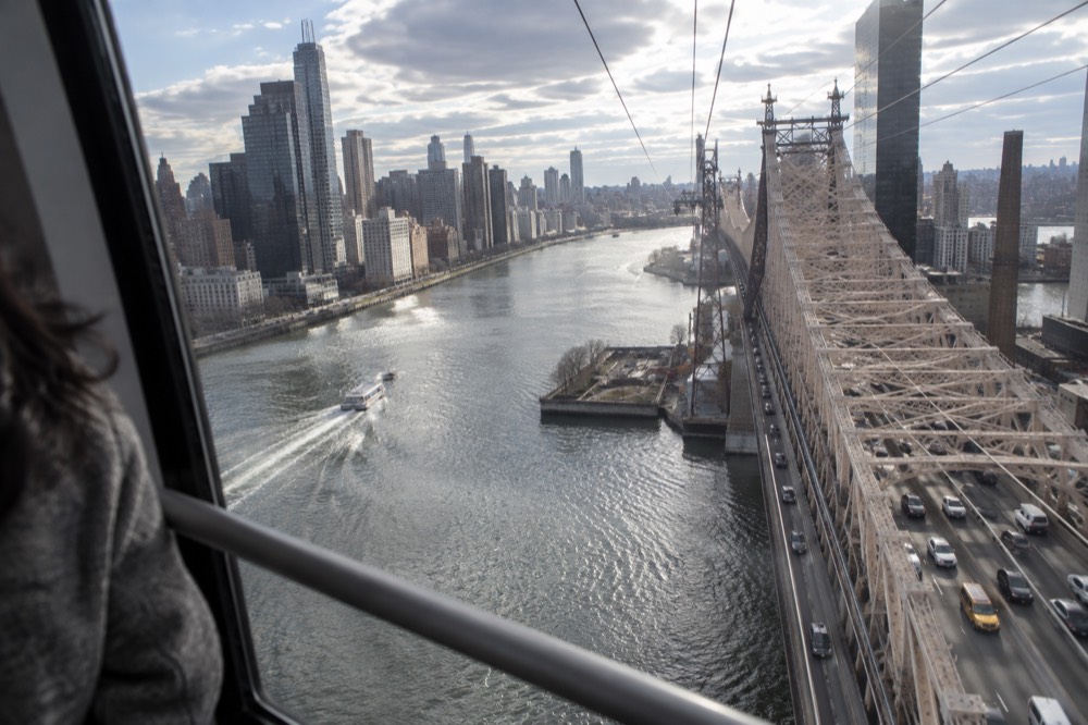 The view from inside a tram cabin looking down at the East River and the Queensboro Bridge roadway below
