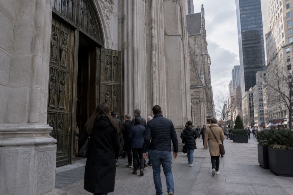 Tourists walking past the bronze doors of St Patrick's Cathedral toward the Fifth Avenue entrance