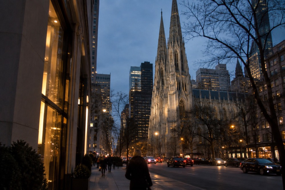 Fifth Avenue at dusk with the cathedral lit against a darkening sky