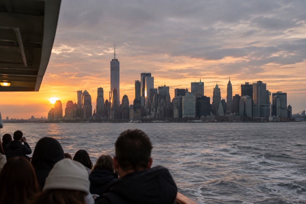 The Manhattan skyline glowing at sunset seen across the harbor from a ferry deck