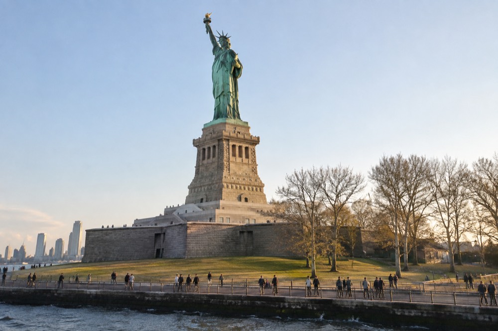 Visitors walking the Liberty Island promenade with the statue rising above them