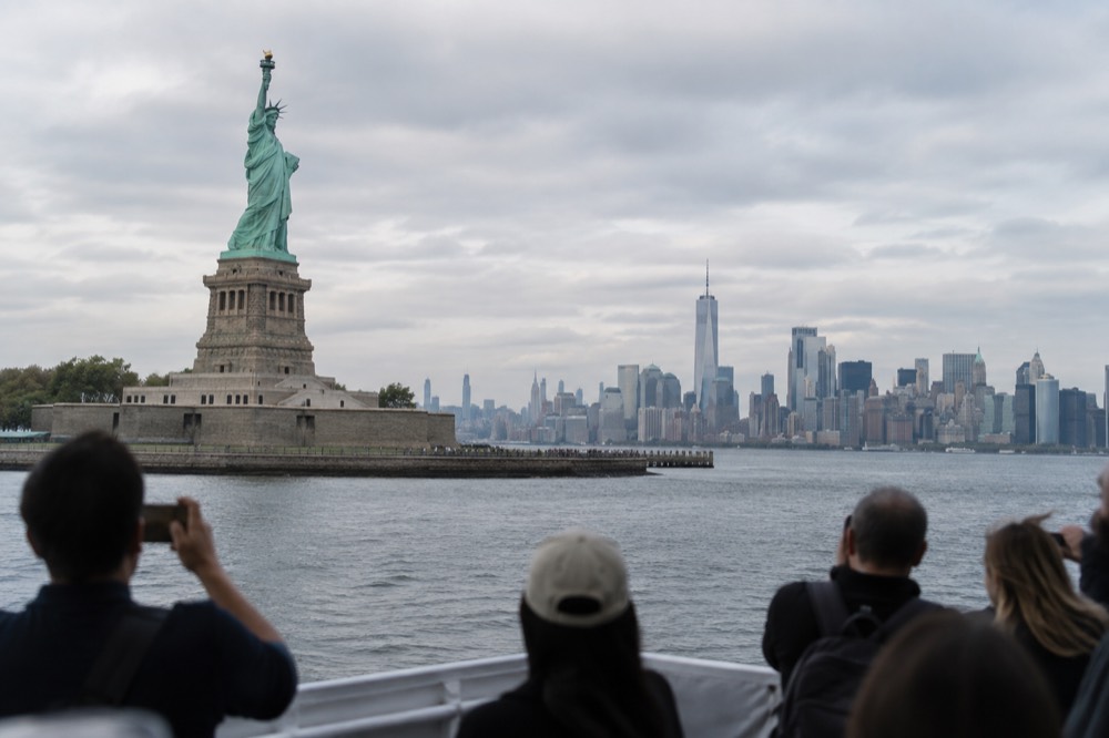 A sightseeing boat passing close to the Statue of Liberty with the Lower Manhattan skyline behind