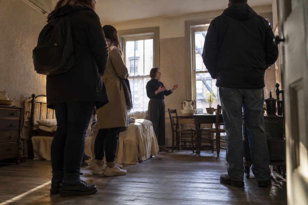 A museum educator speaking to a small group inside a small restored nineteenth-century apartment room
