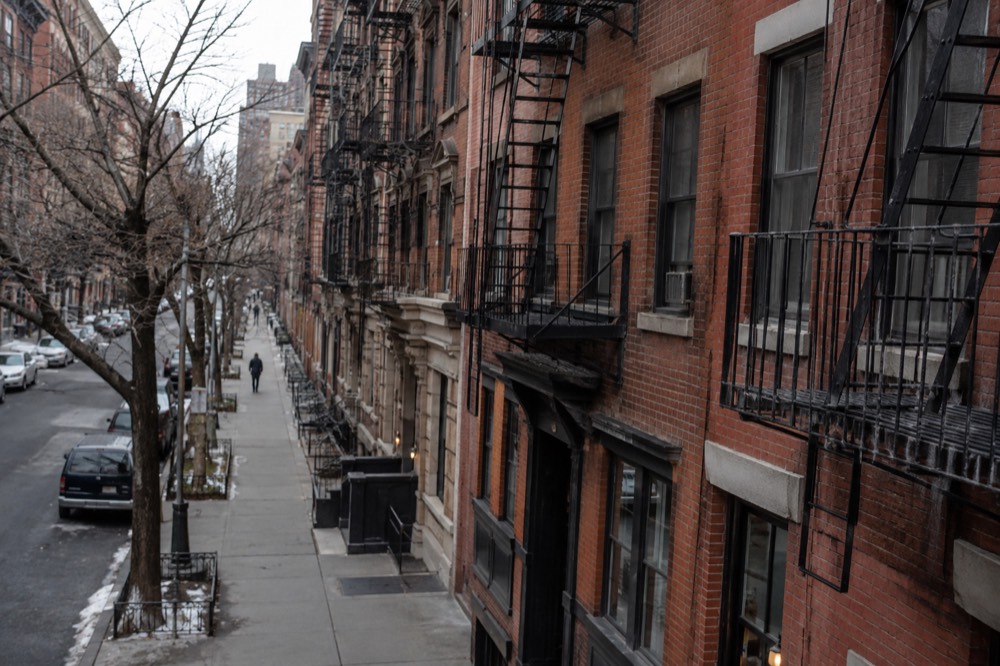 An empty narrow sidewalk in front of old brick apartment buildings on a winter morning