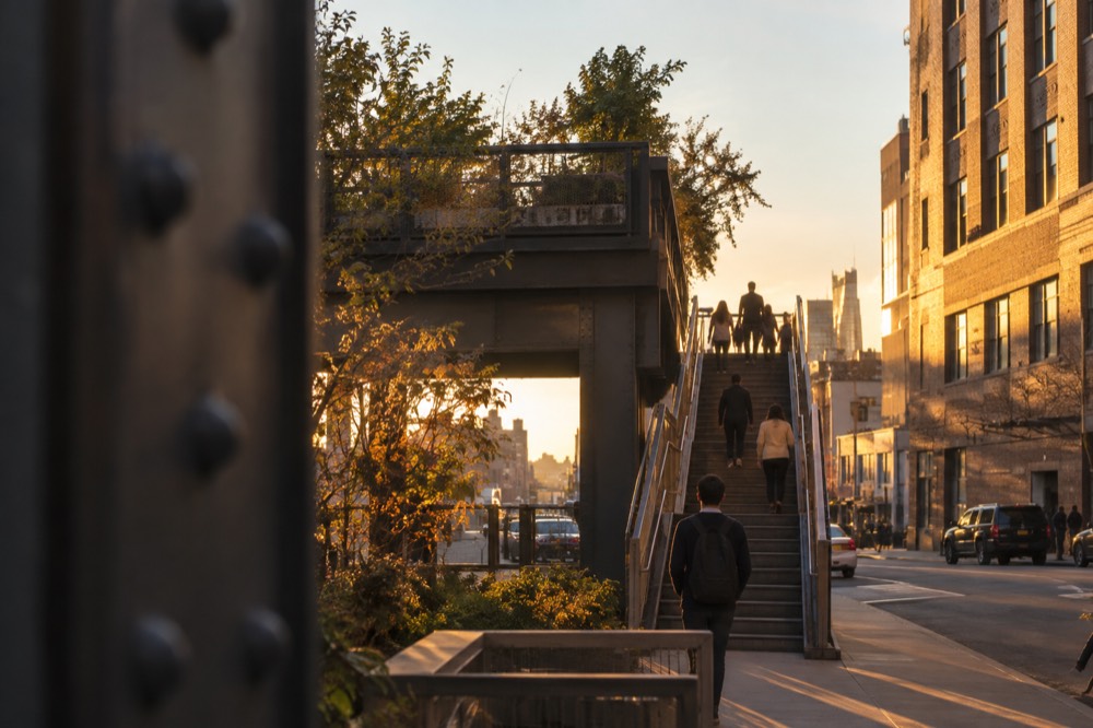 A stair entrance to the High Line rising from a Chelsea street between brick buildings