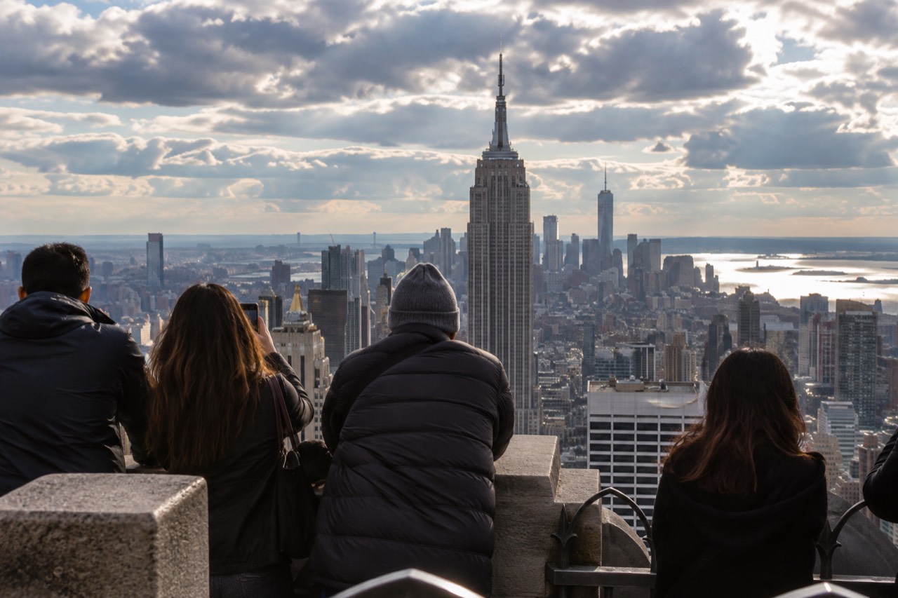 Visitors looking out from the Top of the Rock observation deck toward the Empire State Building and the Manhattan skyline