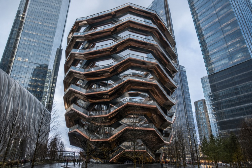 The copper staircases of Vessel seen from below, framed by the glass towers of Hudson Yards