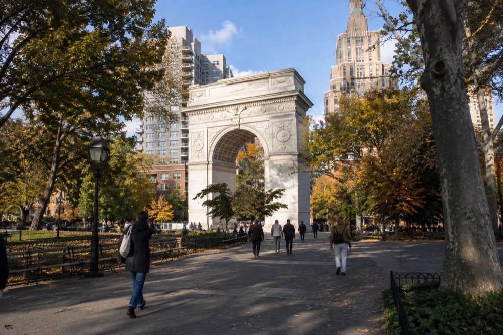 The Washington Arch framed by trees with people walking through the park on a sunny afternoon