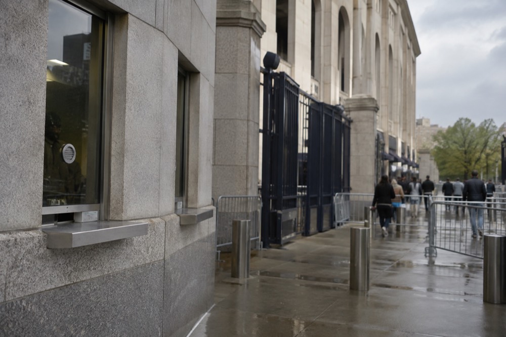 A ticket window and entry gate at Yankee Stadium with visitors checking their phones