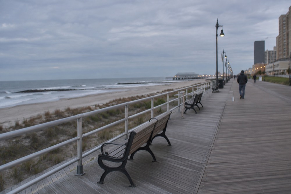 A Boardwalk scene in early autumn with empty benches and calm ocean beyond the railing