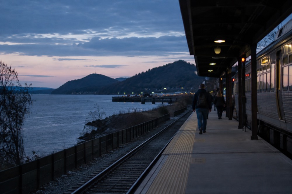 A Metro-North train at a small Hudson Valley station platform beside the river